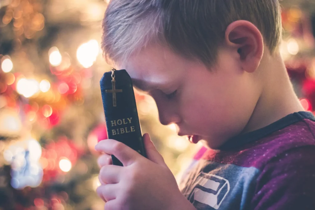 A boy praying and holding a Bible