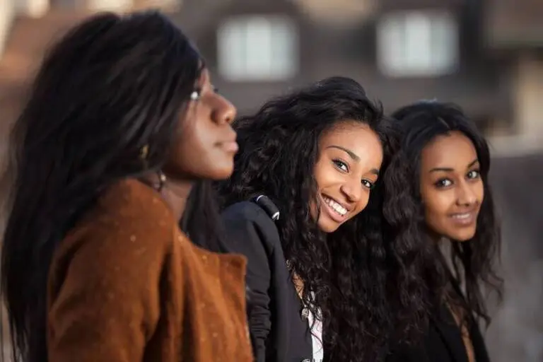 Three black girls, side by side, two are smiling and looking toward the camera, one is looking straight ahead